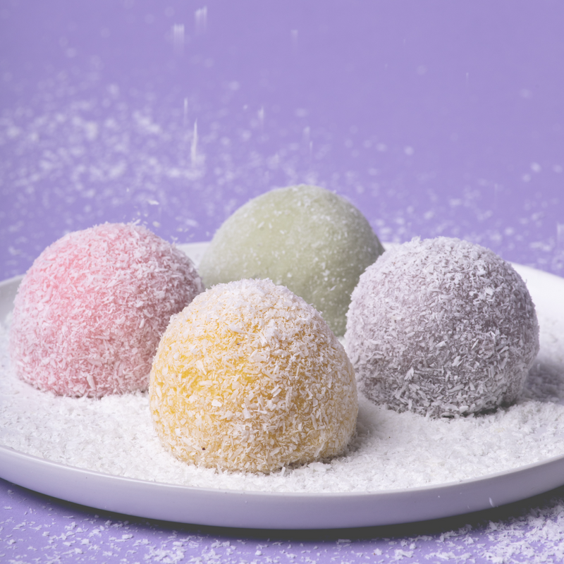 Four round mochis topped with coconut flakes sit atop a white plate.